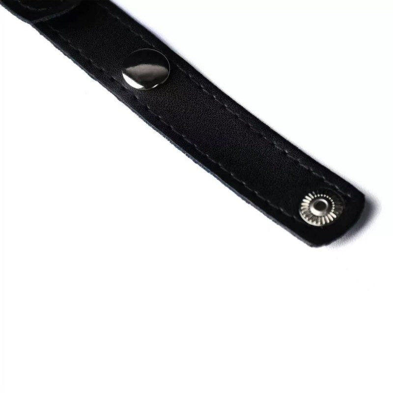 Close-up of the snap fastener and stitching on a black faux-leather strap